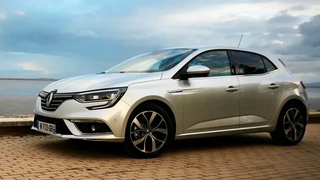 Plateado Renault Megane con modernos motores, aparcado junto al mar con un cielo nublado.