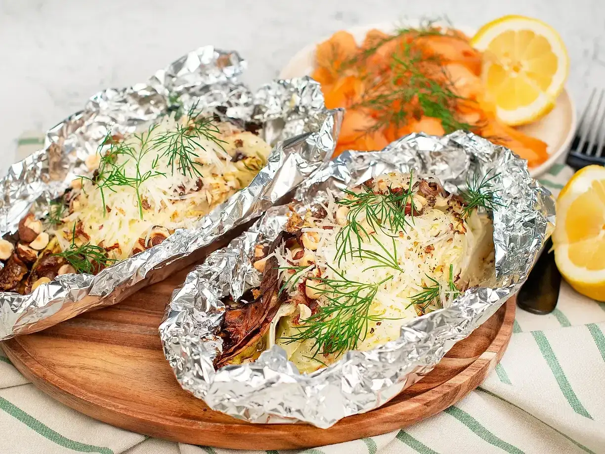 Två portioner ugnsbakad spetskål i folie, toppad med ost, nötter och dill. Serveras med rökt lax och citronklyftor.