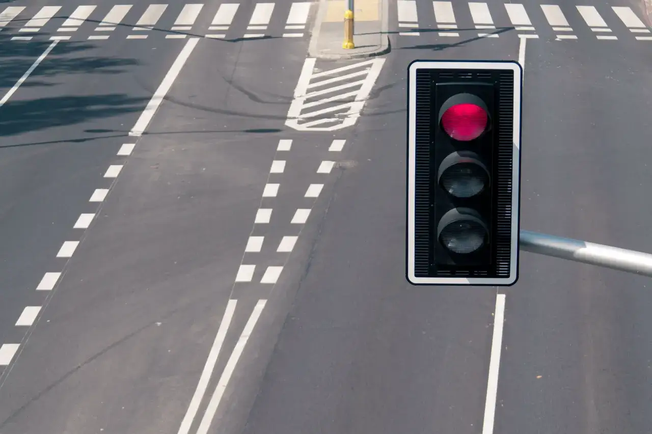Czerwone światło sygnalizatora na skrzyżowaniu. Widoczne pasy dla pieszych i jezdnia. R&oacute;żne rodzaje kamer na skrzyżowaniach mogą monitorować ruch.