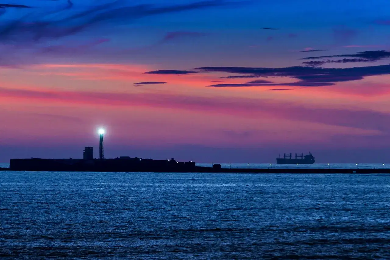 Espectacular puesta de sol en Cádiz con el faro iluminado y un carguero navegando.