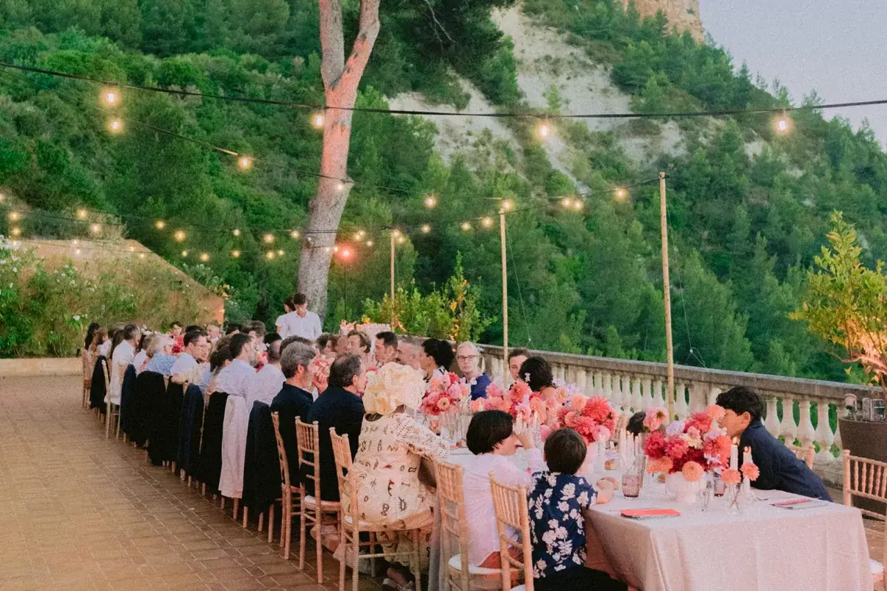 Une longue table dress&eacute;e pour un mariage en ext&eacute;rieur, &eacute;clair&eacute;e par des guirlandes lumineuses. Une animation surprise est sur le point de commencer.