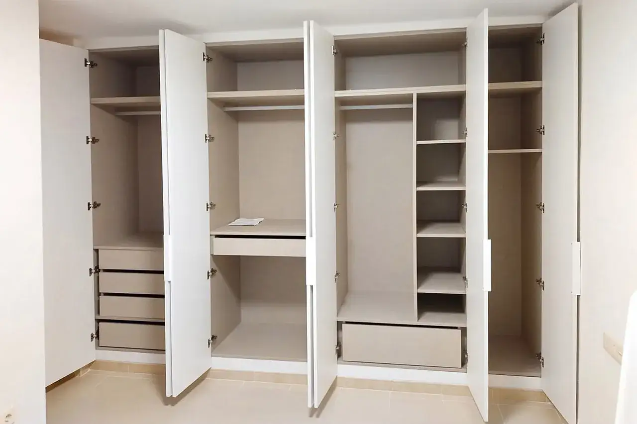Armario empotrado con puertas abiertas, mostrando estantes, cajones y barras para colgar. Perfecto para forrar armario empotrado y organizar tu ropa.