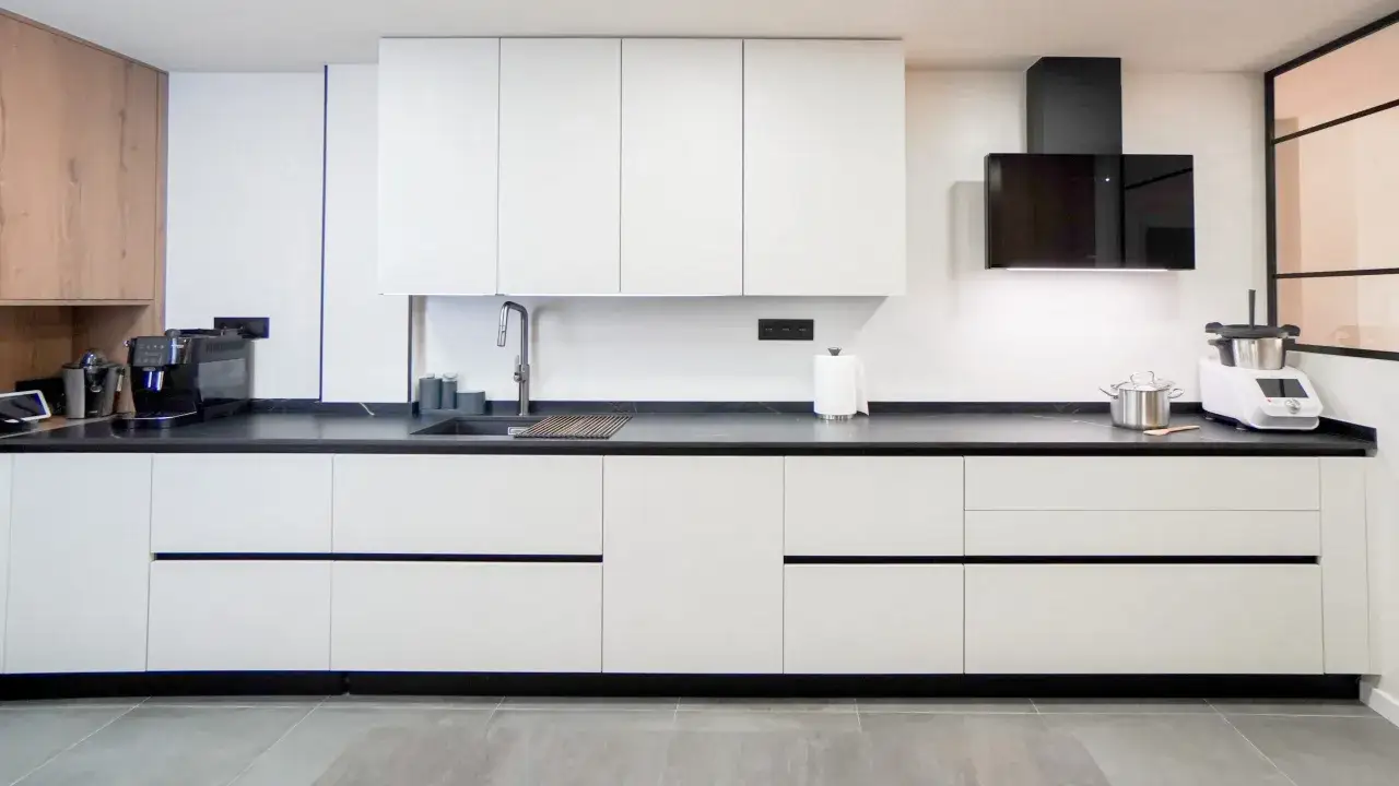 Cocinas modernas blancas con encimera oscura, campana extractora negra y electrodom&eacute;sticos.
