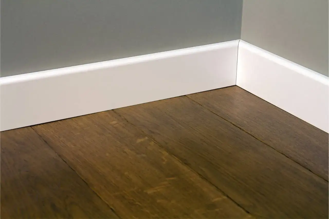 Esquina de una habitación con suelo de madera oscura y rodapiés blancos modernos. Hay varios tipos de rodapiés, y este es un ejemplo minimalista.