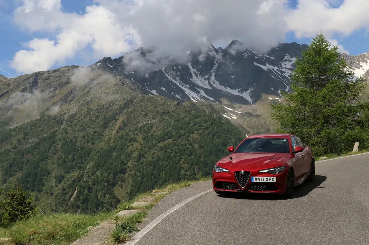 Un Alfa Romeo Giulia rojo en una carretera de monta&ntilde;a, listo para una prueba alfa romeo giulia. El paisaje alpino es impresionante.