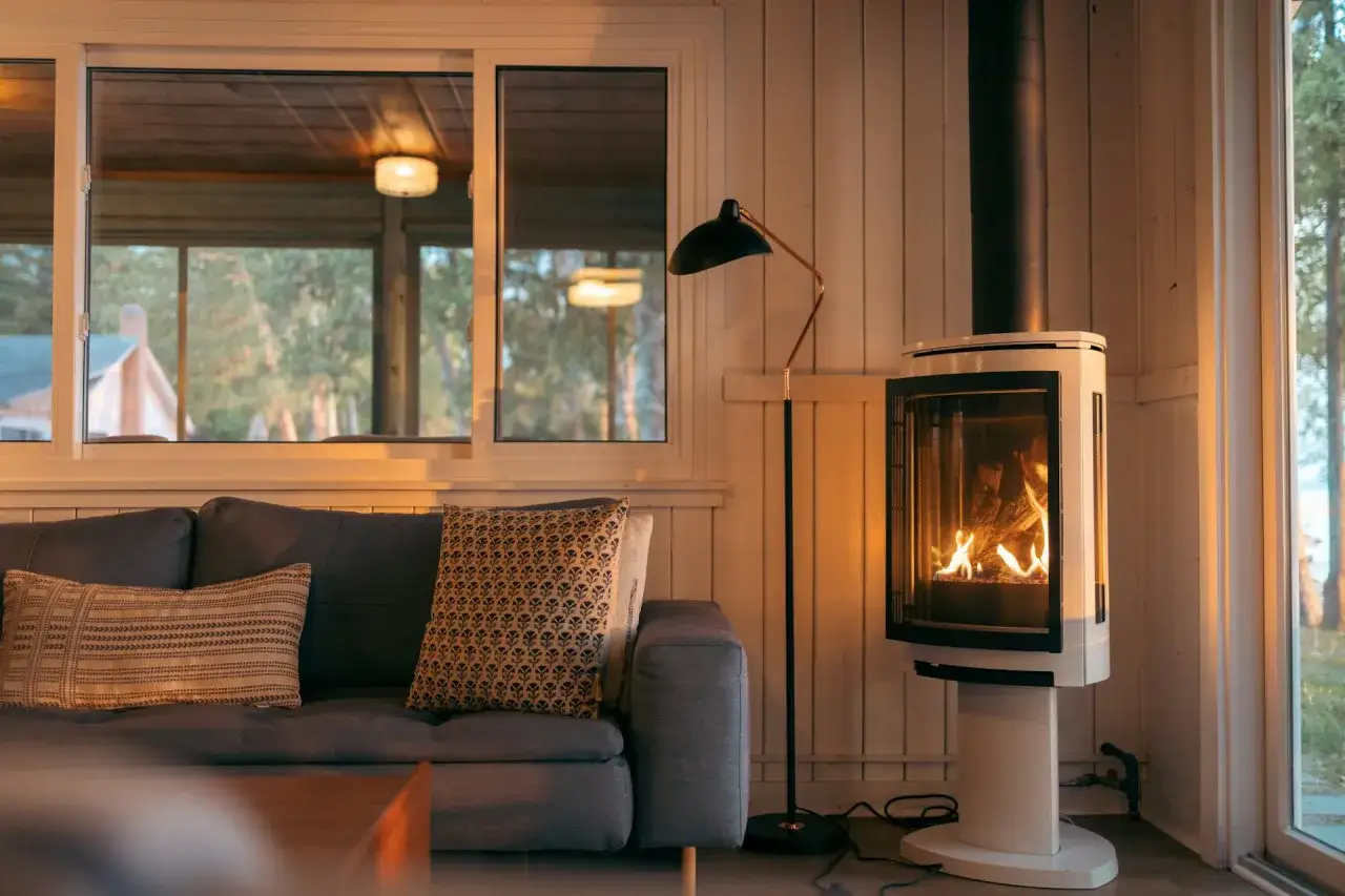 Un poêle à bois moderne crépite, invitant à respecter la distance à respecter autour d'un poêle à bois pour un confort sûr. Un canapé douillet et une fenêtre lumineuse complètent la scène.