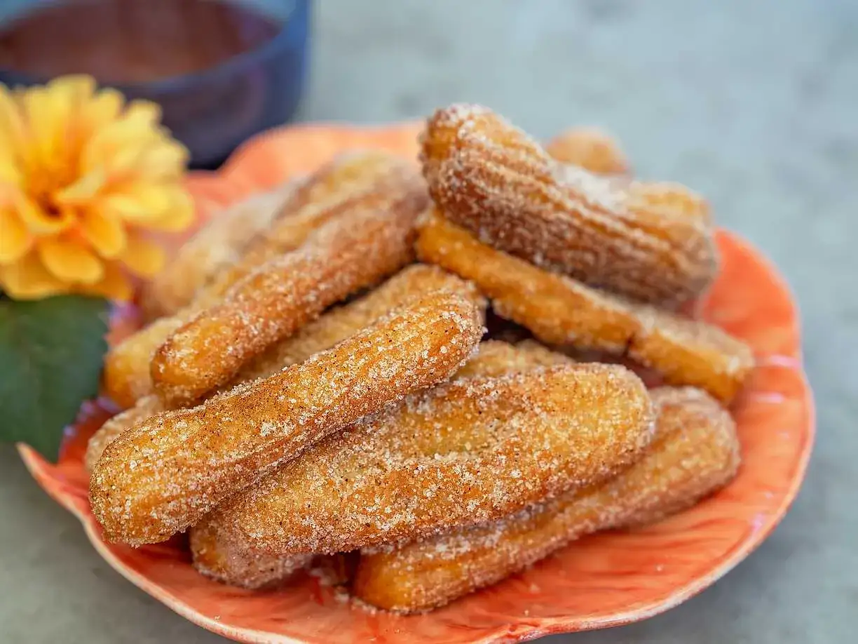 En tallrik med gyllene, socker- och kaneldr&auml;nkta churros, redo att avnjutas. Ett perfekt churros recept f&ouml;r hemmabruk.