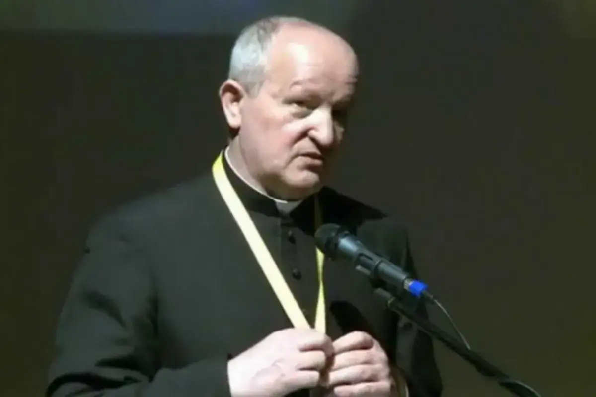 Duchowny w sutannie z żółtą wstęgą przemawia przy mikrofonie. Może to być część uroczystości odpustowej.