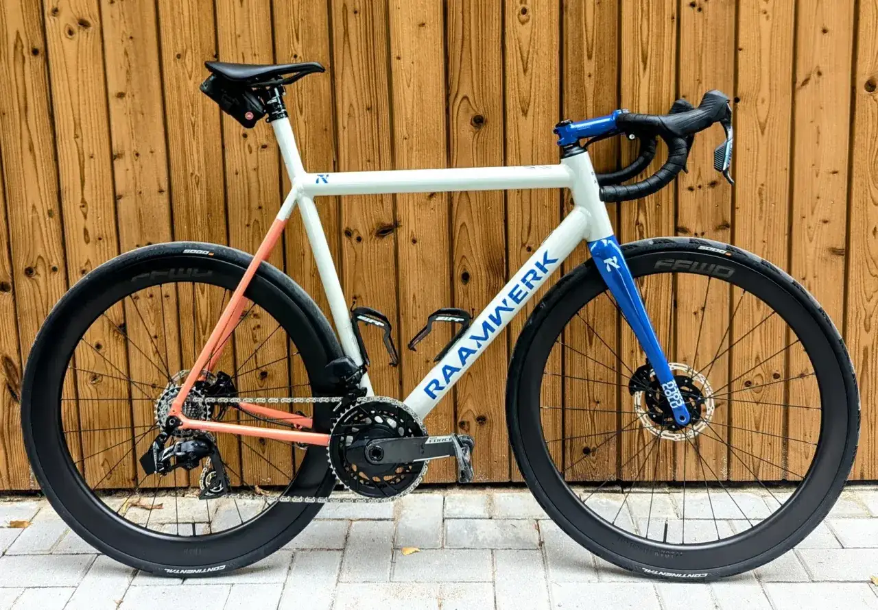 Een witte RAAMWERK racefiets met blauwe en oranje accenten. Deze carbon racefiets is klaar voor elke rit.