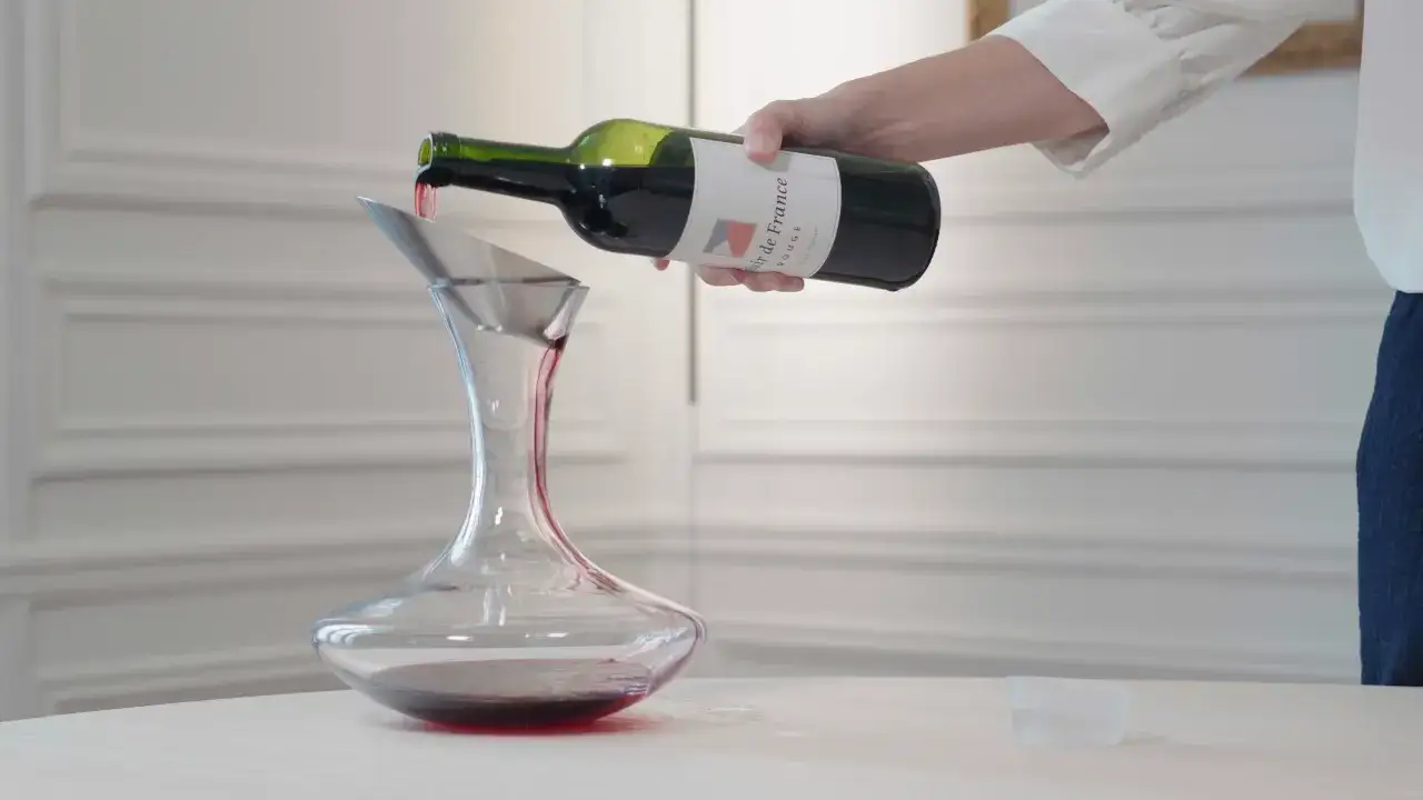 Eine Hand gießt Rotwein aus einer Flasche in einen Dekanter. Der Wein wird durch einen silbernen Trichter geleitet, um ihn zu belüften, bevor er verkorkt wird.