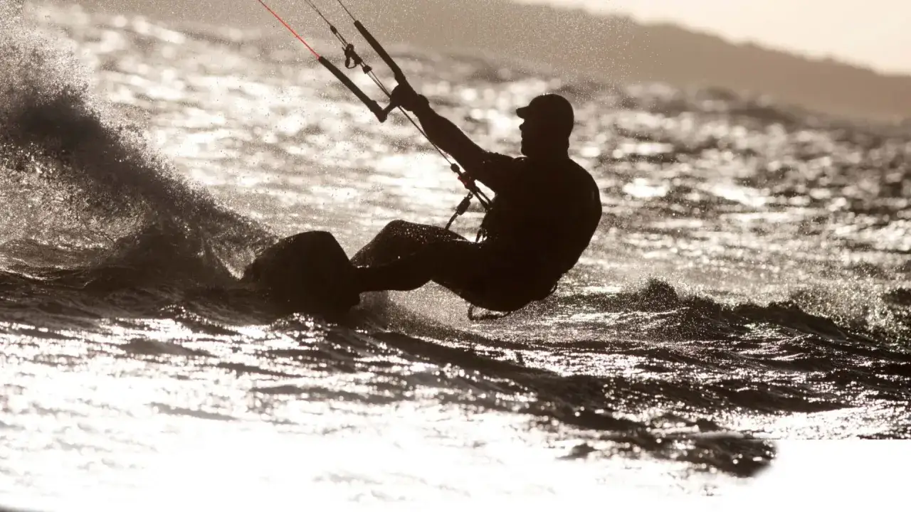 Kitesurfare i solnedg&aring;ngen, en silhuett mot glittrande vatten. En perfekt dag f&ouml;r att surfa i Sverige.