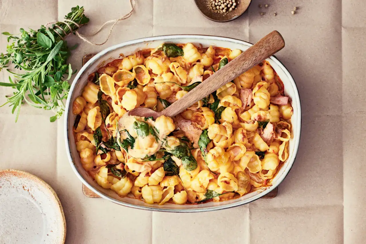 En krämig pastarätt med spenat och skinka, perfekt för nyttiga recept. En träsked lyfter upp en portion ur ugnsformen.