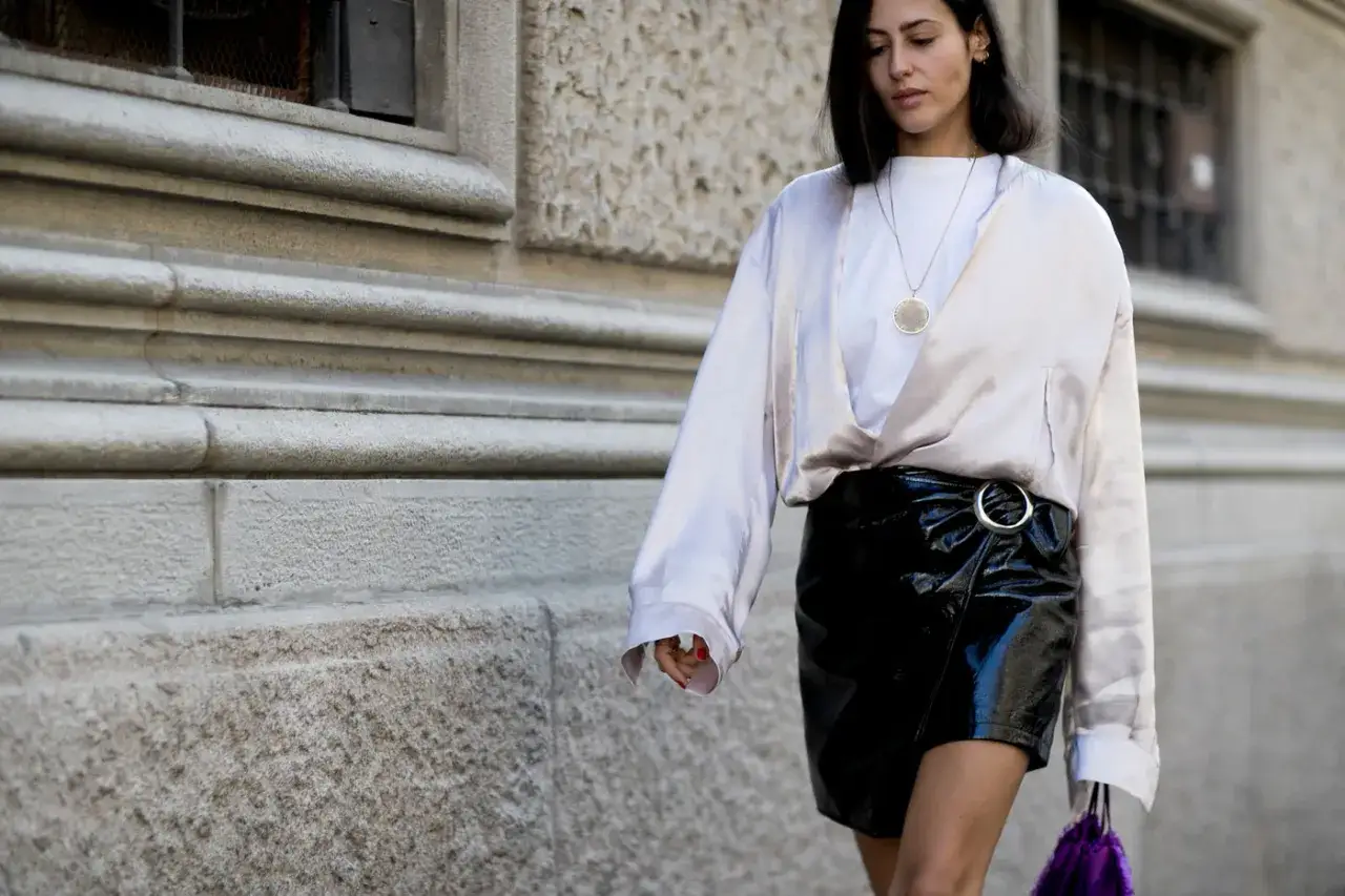 Modna it girl w satynowej bluzce i lakierowanej spódniczce, z fioletową torebką.