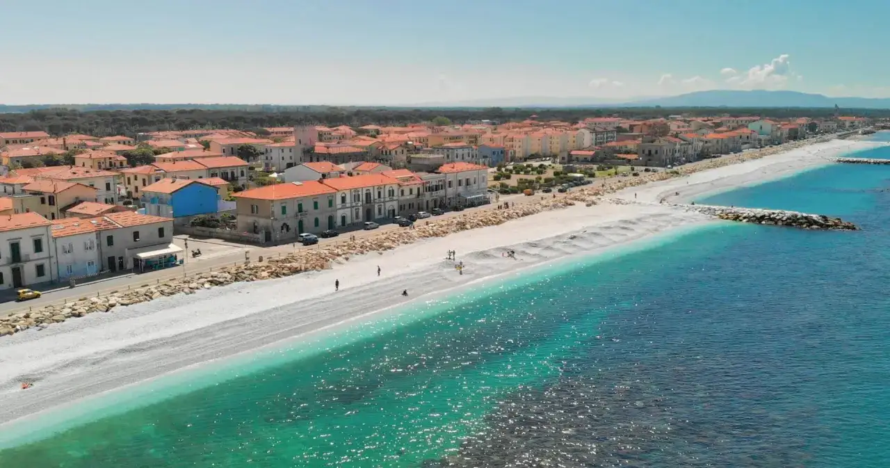 Idealne toskania wakacje: biała plaża, turkusowe morze i urokliwe miasteczko z pomarańczowymi dachami.
