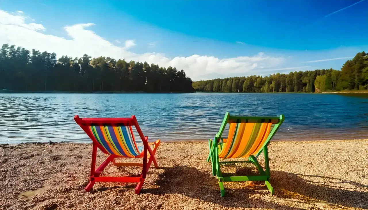 Dwa kolorowe leżaki na piaszczystej plaży nad jeziorem Niesłysz. W tle las i błękitne niebo.