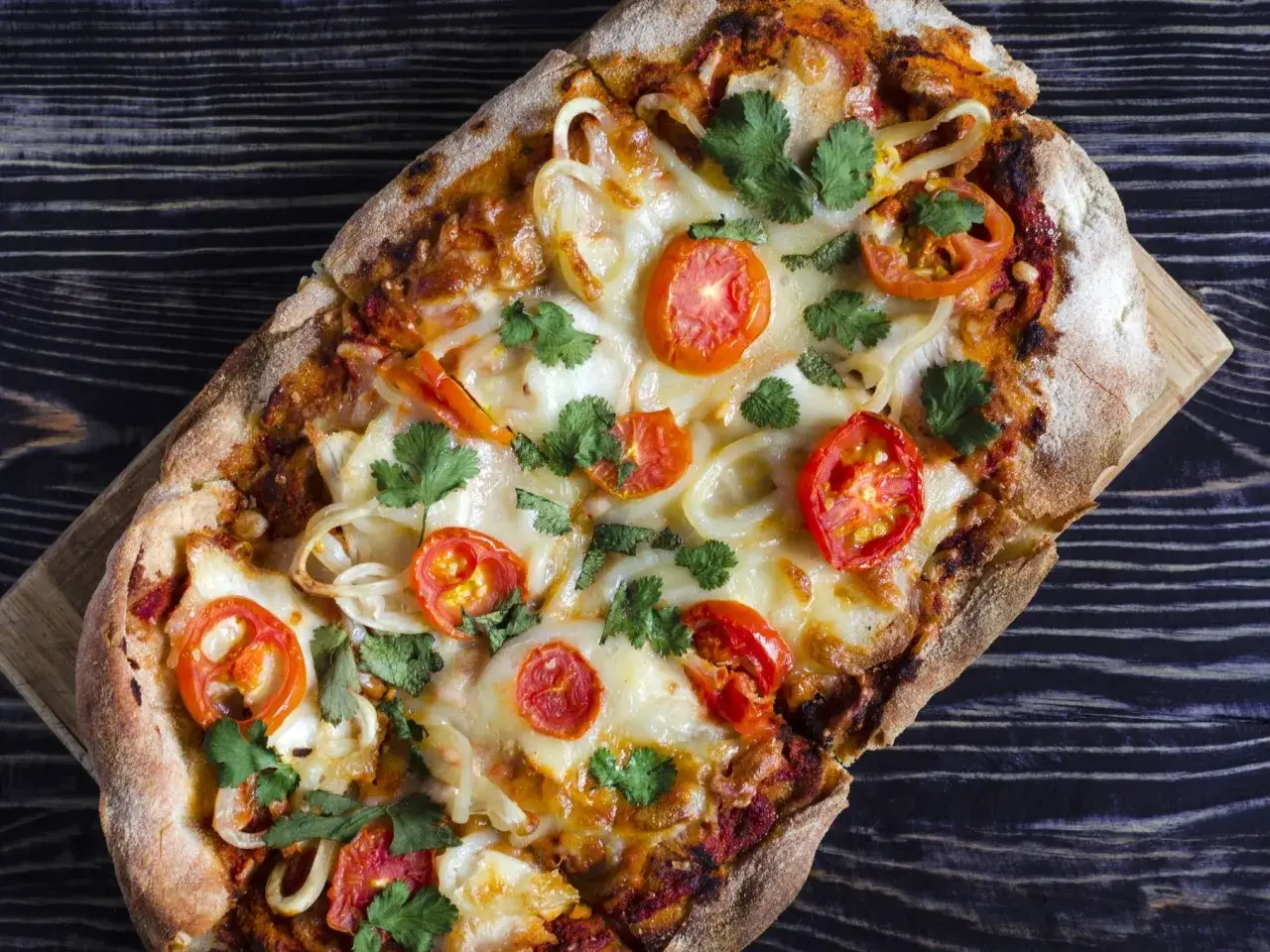 Eine rechteckige Pinsa mit Tomaten, Zwiebeln und Käse, garniert mit Koriander. Die Pinsa herkunft liegt in der römischen Tradition.