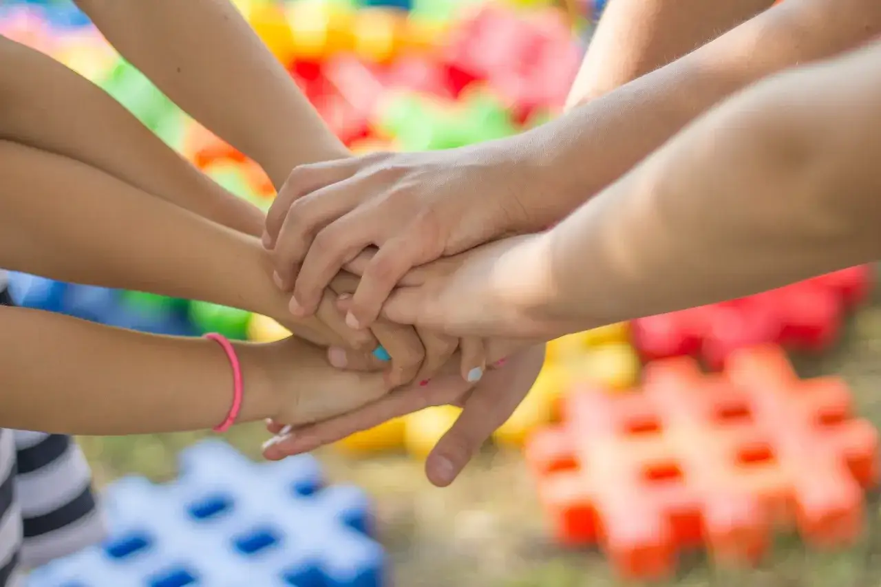 Dzieci klas 1-3 łączą ręce, symbolizując wspólne zabawy integracyjne. W tle kolorowe klocki.
