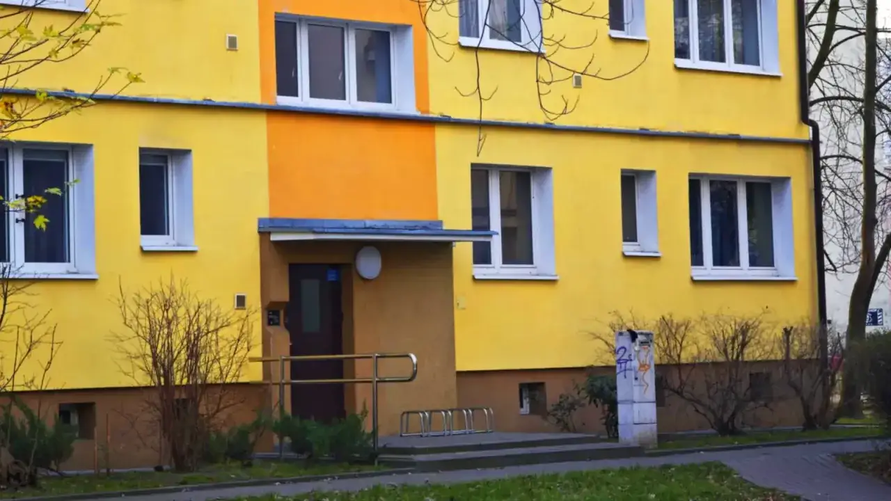 Jasnożółty blok z pomarańczowym akcentem. Przed wejściem stojaki na rowery. Warto pamiętać o terminowym opłaceniu czynszu administracyjnego.
