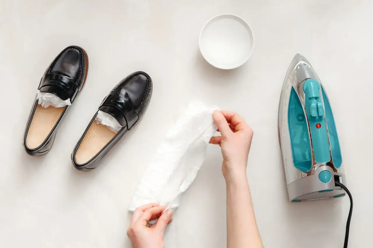 Schwarze Lederschuhe werden mit einem feuchten Tuch und einem Bügeleisen behandelt, um Falten aus lederschuhen zu entfernen.