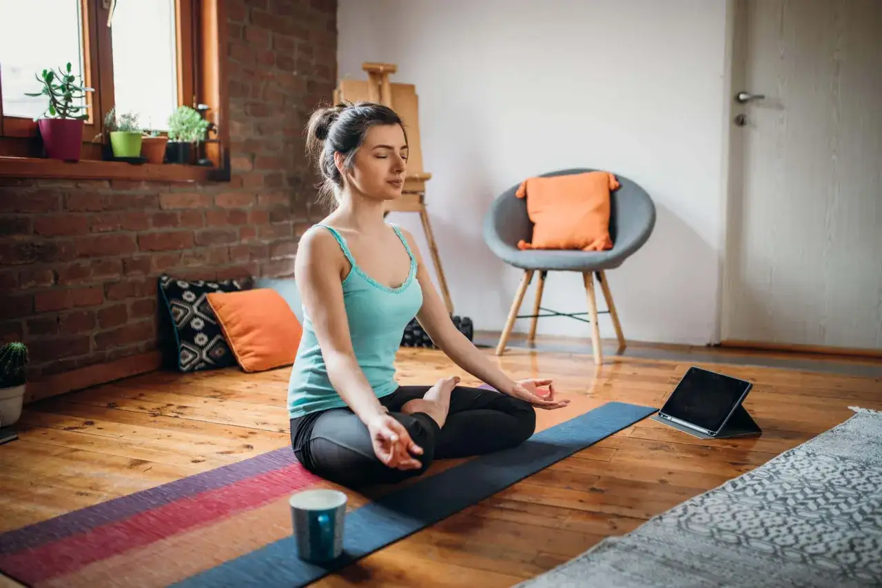 Kvinna med slutna ögon mediterar på en yogamatta, följer en gratis yoga app på en surfplatta.