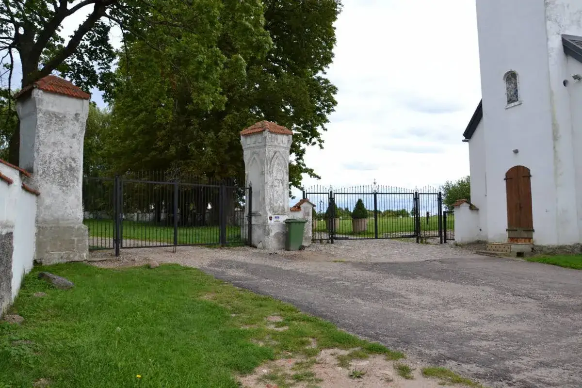 Brama wjazdowa do starzyński dw&oacute;r, z kamiennymi słupami i kutym ogrodzeniem. W tle drzewa i biały budynek.