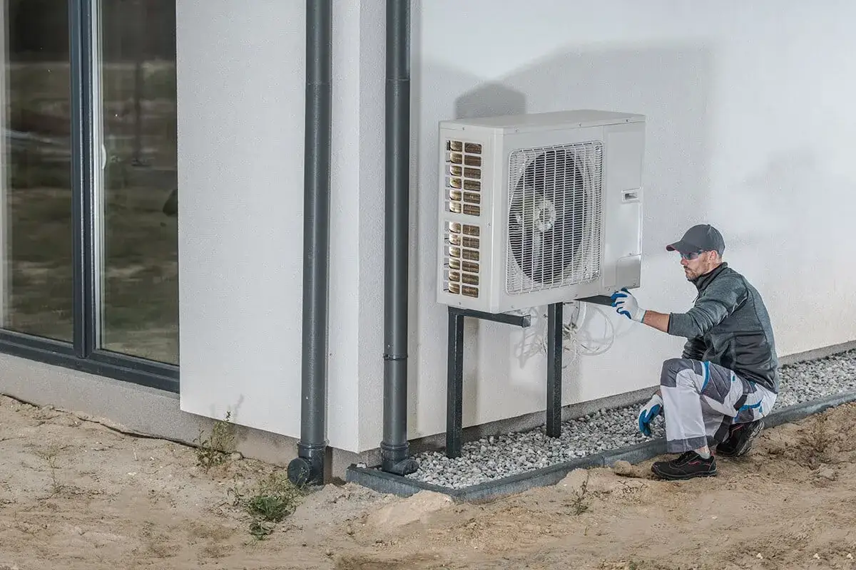 Un technicien v&eacute;rifie une pompe &agrave; chaleur ext&eacute;rieure. L'installation est soign&eacute;e, sugg&eacute;rant une bonne dur&eacute;e de vie pour l'appareil.