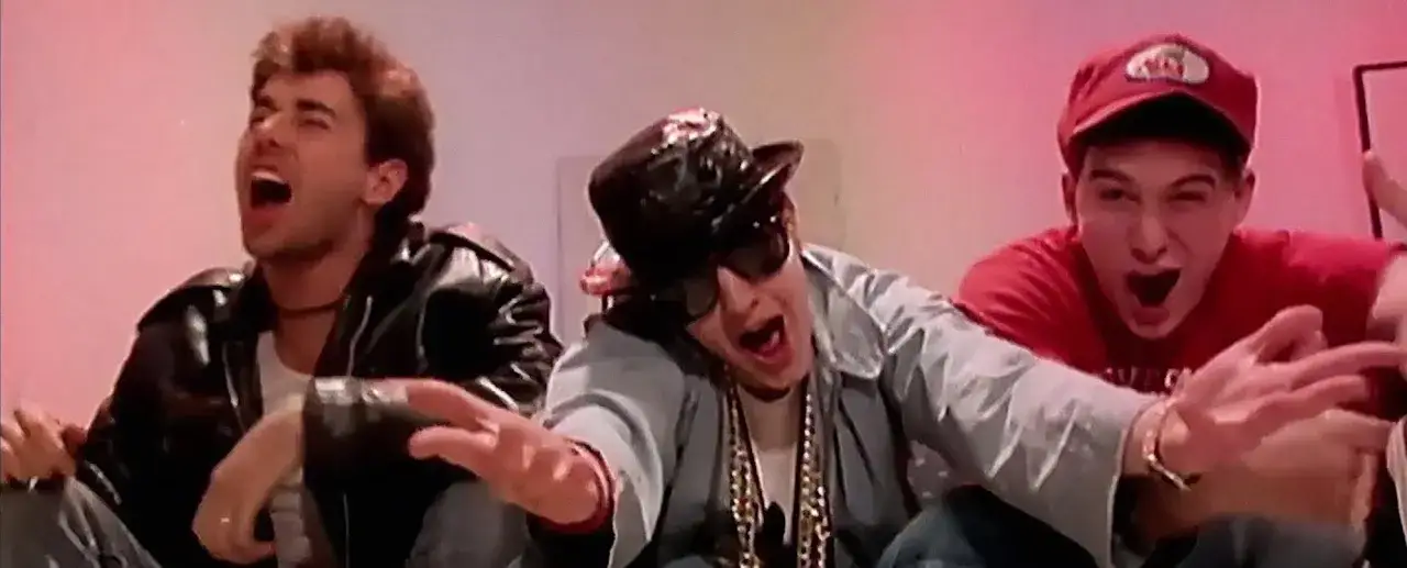 Trois amis, un rappeur année 80 au milieu avec chapeau et lunettes, chantent avec énergie.