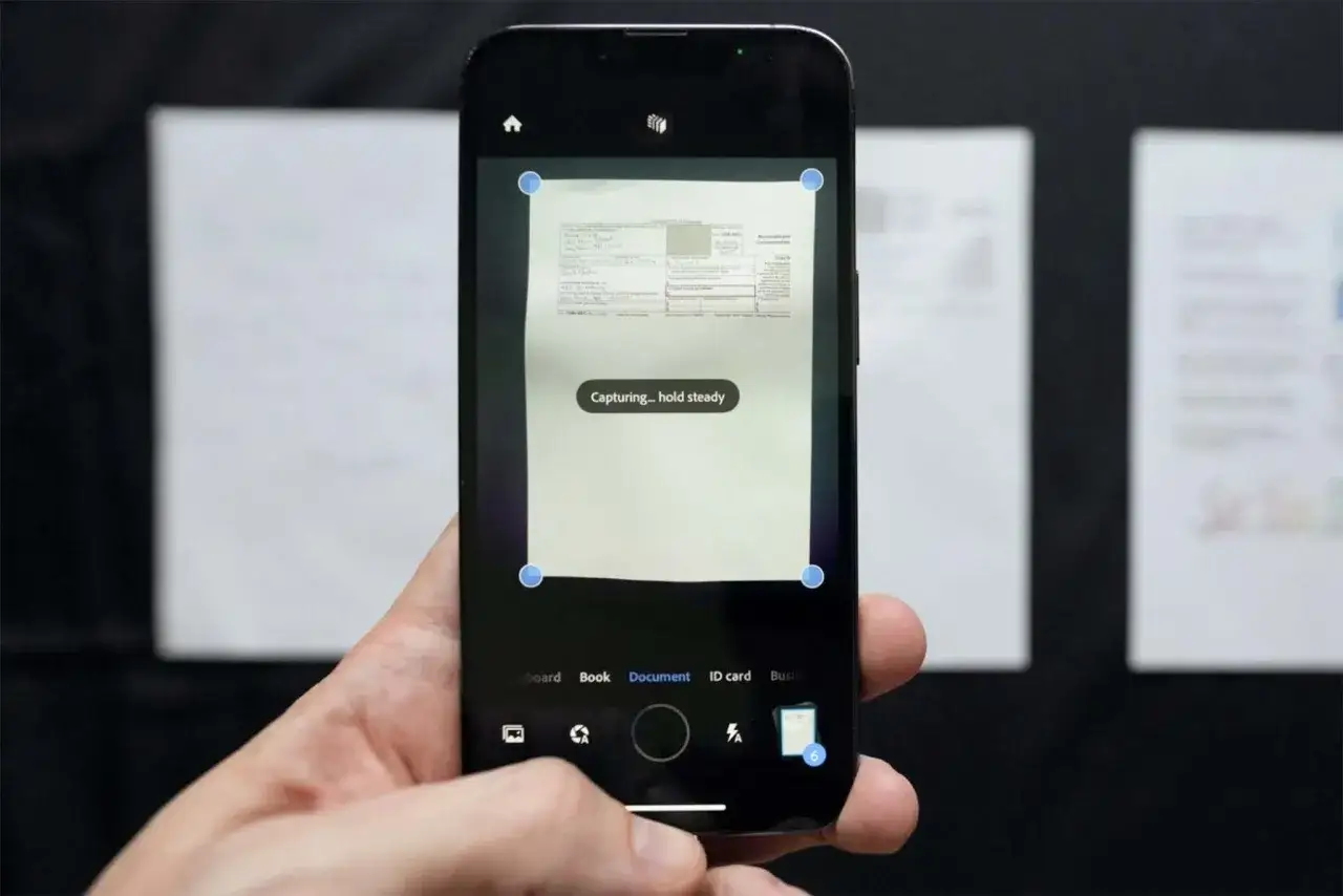 Un smartphone capture un document avec une application de **genius scan**. L'écran affiche