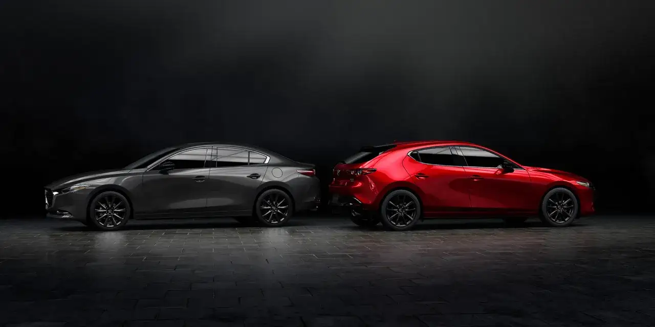 Szary Mazda 3 sedan i czerwony hatchback stoją obok siebie na ciemnym tle.