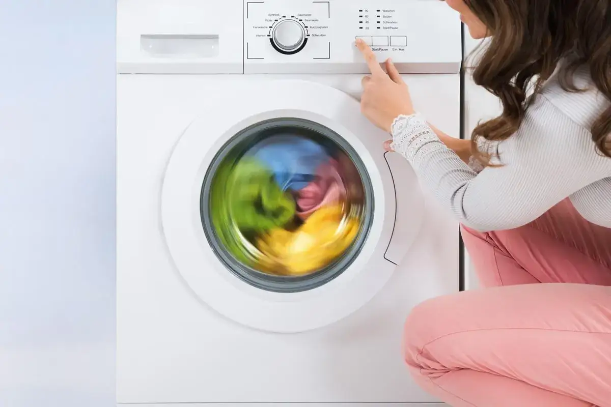 Donna avvia la lavatrice. La centrifuga restringe i capi, creando un vortice di colori vivaci all'interno del cestello.