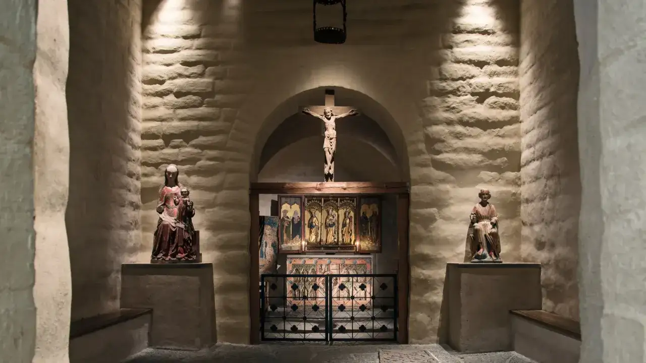 En kyrka från medeltiden med en korsfäst Kristusfigur ovanför ett altarskåp. Statyer av Maria och ett helgon flankerar utrymmet.