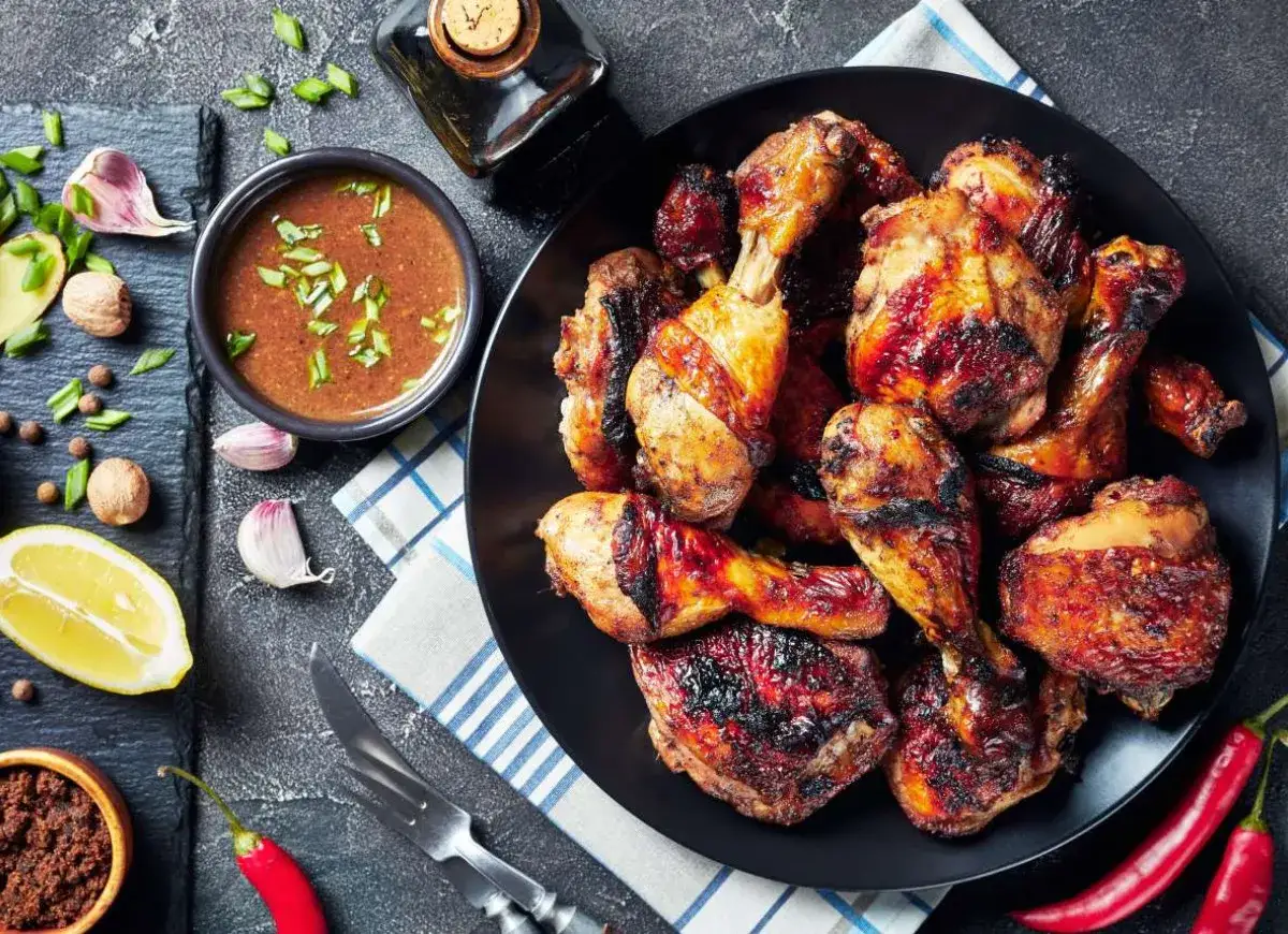 Pyszny kurczak z grilla na czarnym talerzu, podany z sosem, cytryną i papryczkami chili.