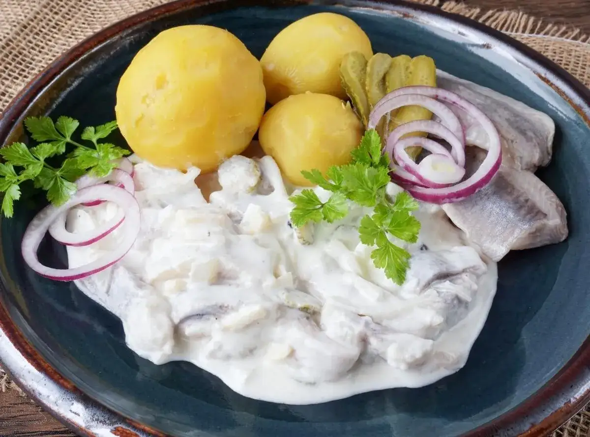 Marinierter Hering in cremiger Soße mit Salzkartoffeln, Gurken und Zwiebelringen. Ein klassisches Gericht, das auf keiner Tafel fehlen darf.