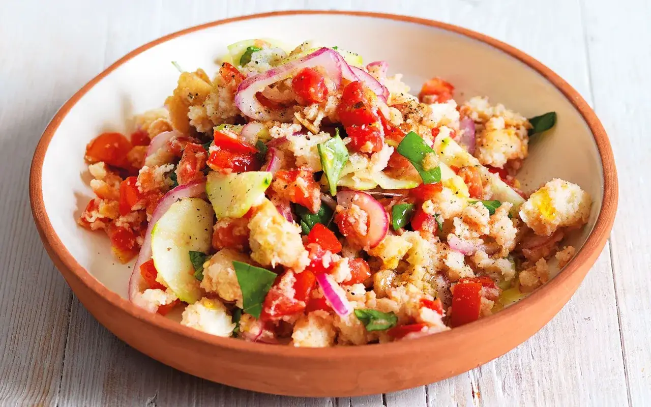 Panzanella ricetta: un'insalata estiva con pane raffermo, pomodori, cetrioli, cipolla rossa e basilico, condita con olio d'oliva.