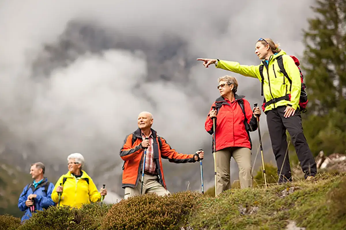 Une accompagnatrice en reconversion moyenne montagne montre le chemin &agrave; un groupe de randonneurs.