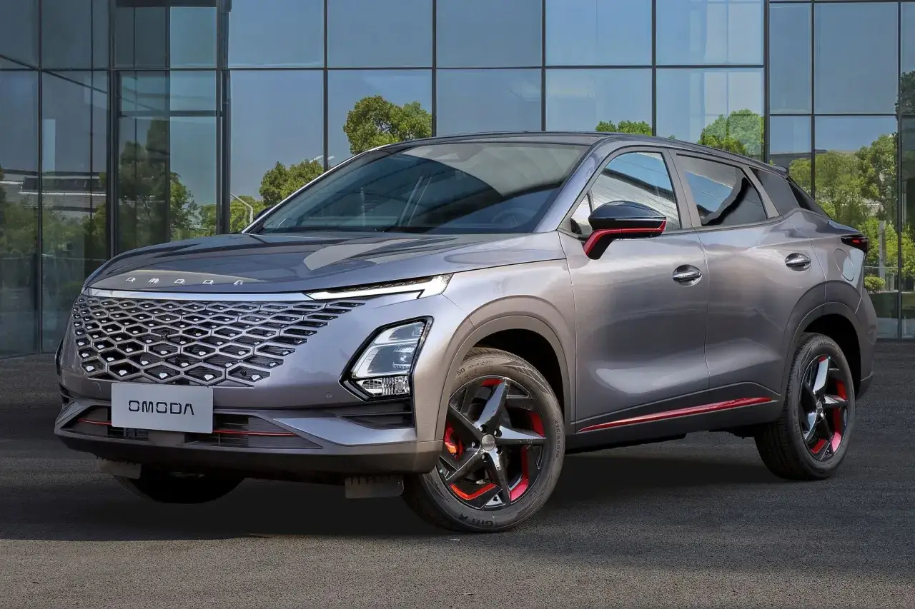 Szary OMODA C5, sportowy SUV z czerwonymi akcentami, zaparkowany przed nowoczesnym budynkiem.