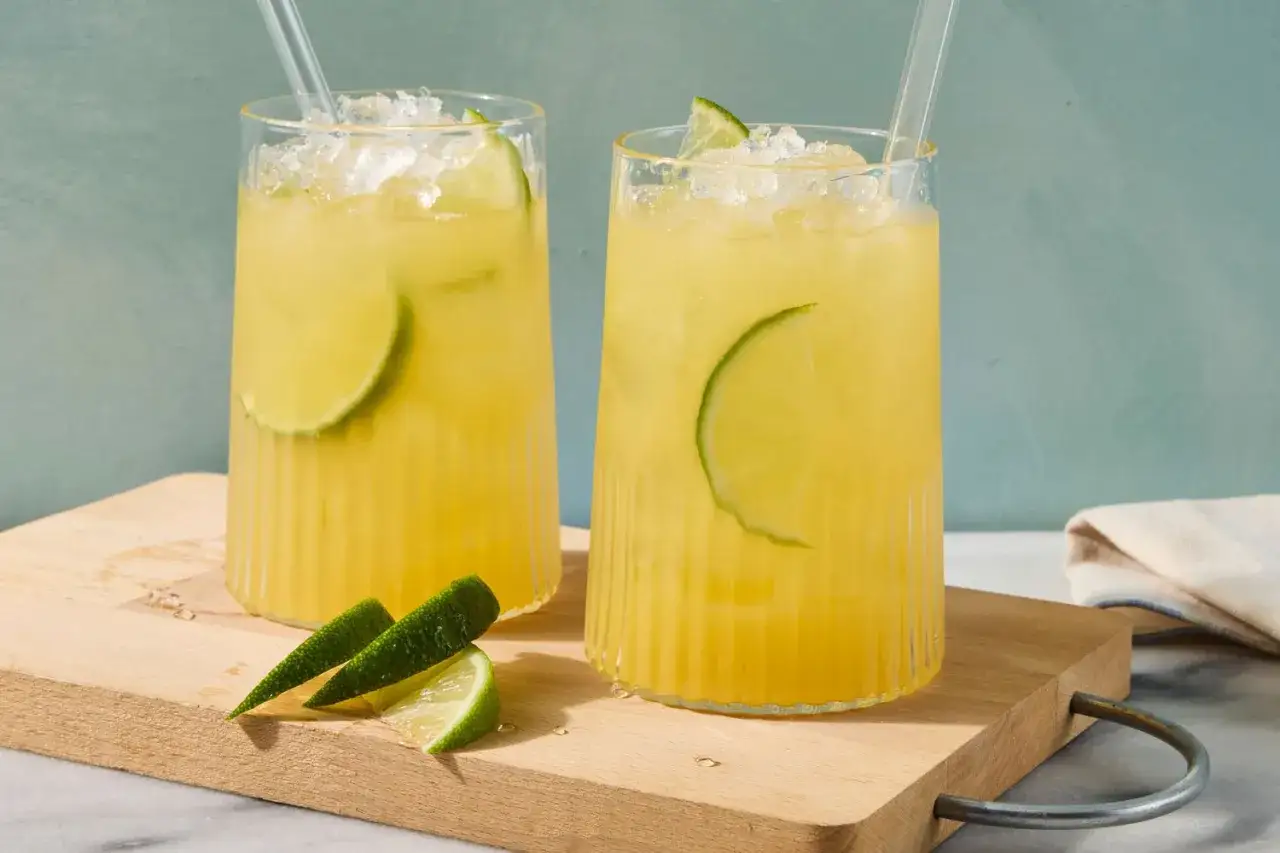 Deux verres de boisson énergisante maison, remplis de glaçons et de rondelles de citron vert, sur une planche en bois.