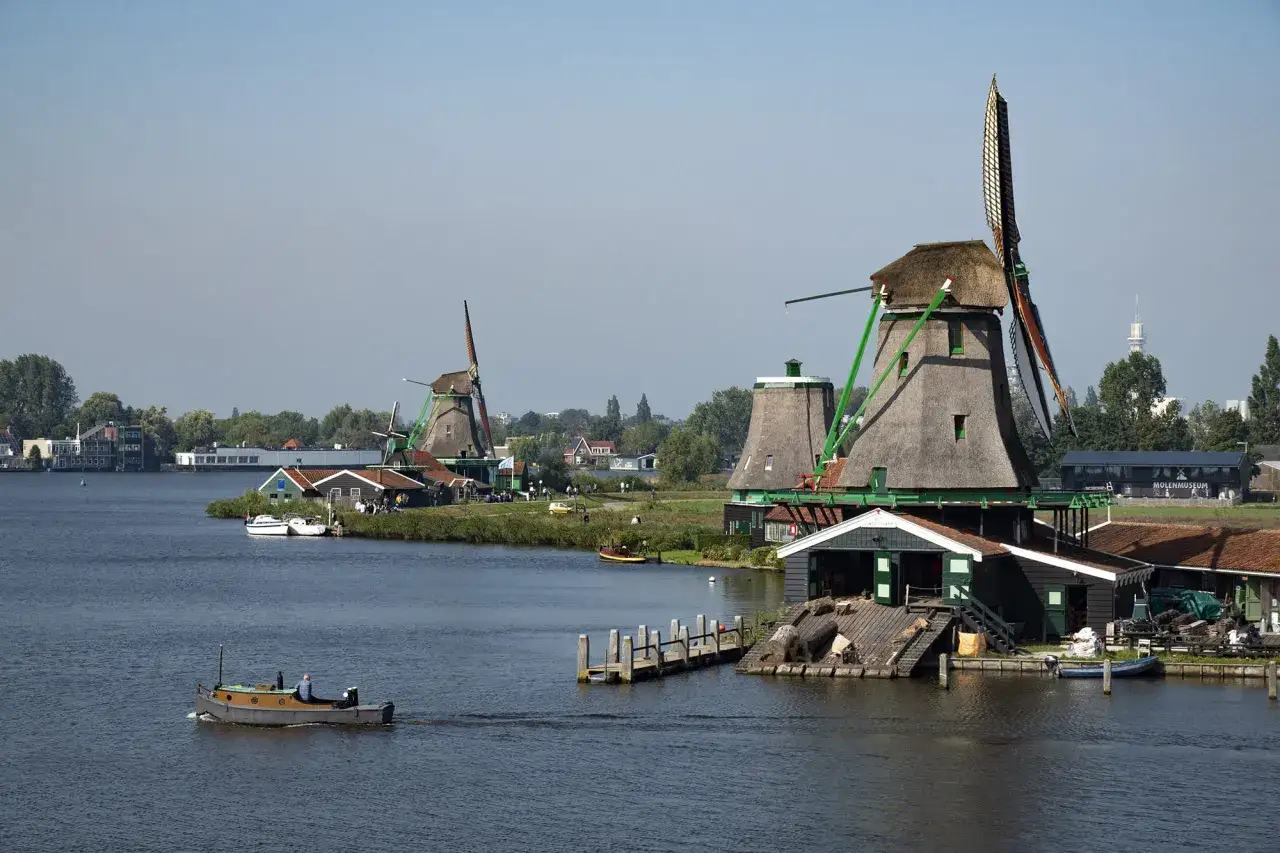 Moulins à vent emblématiques, un bateau naviguant sur l'eau, un paysage incontournable des Pays-Bas.