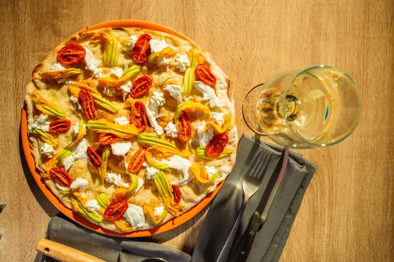 Deliciosa pizza tonda romana con flores de calabacín, tomates secos y queso fresco. Un festín para los sentidos.