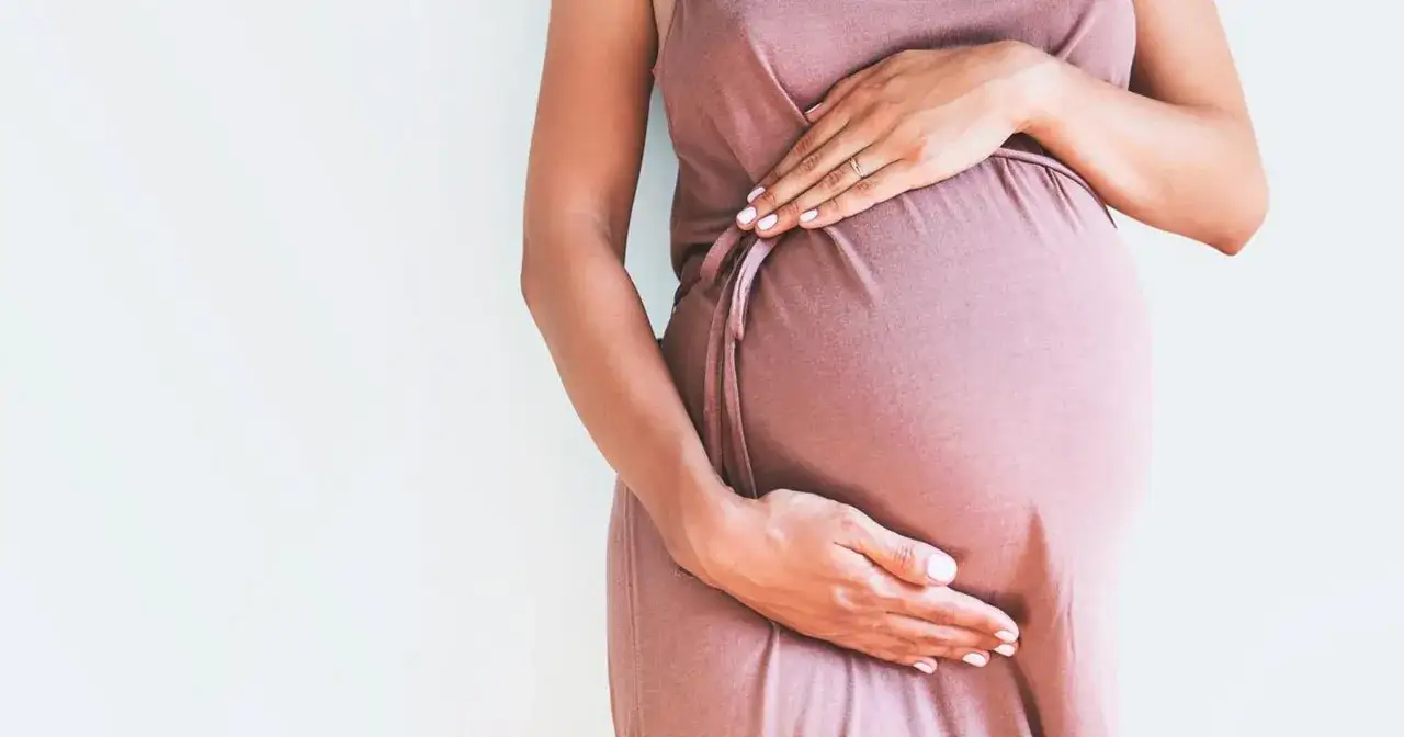 Brzuch kobiety w ciąży, kt&oacute;ra schudła w ciąży 10 kg. Dłonie delikatnie obejmują zaokrąglony brzuch.