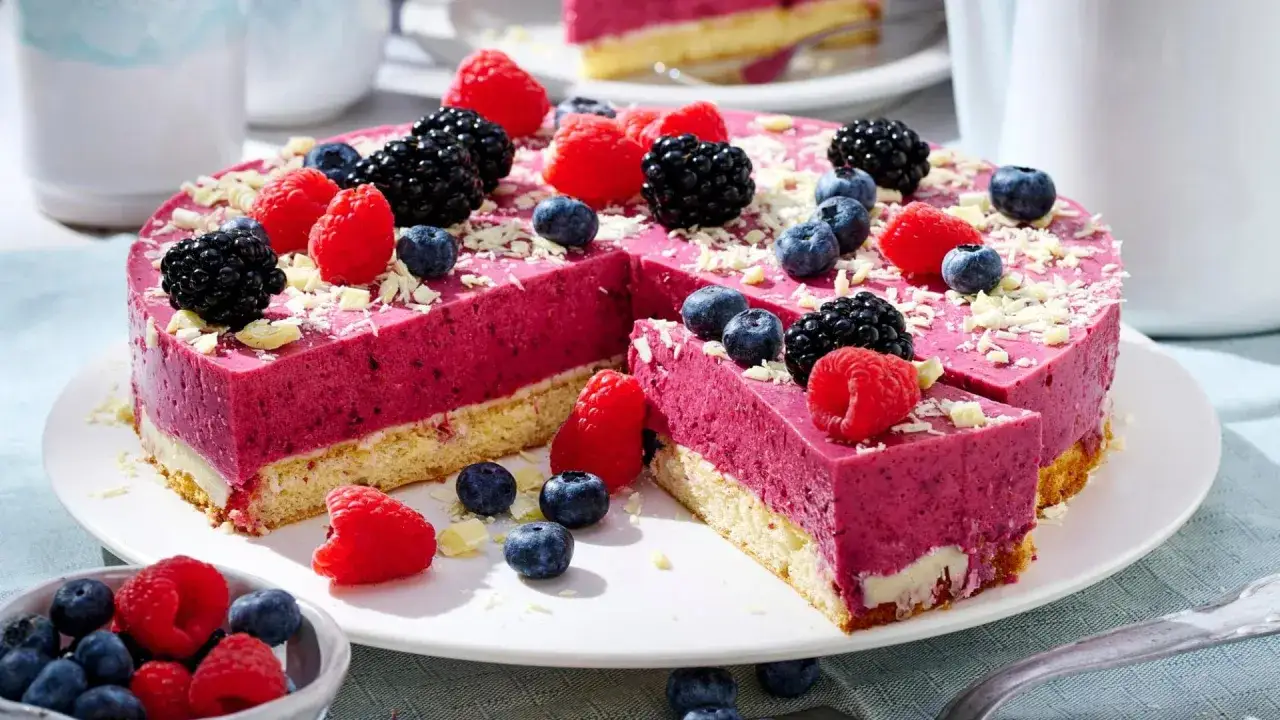 Ein erfrischender Sommerkuchen mit Beeren und weißer Schokolade. Saftige Himbeeren, Brombeeren und Blaubeeren zieren die pinke Mousse-Schicht.