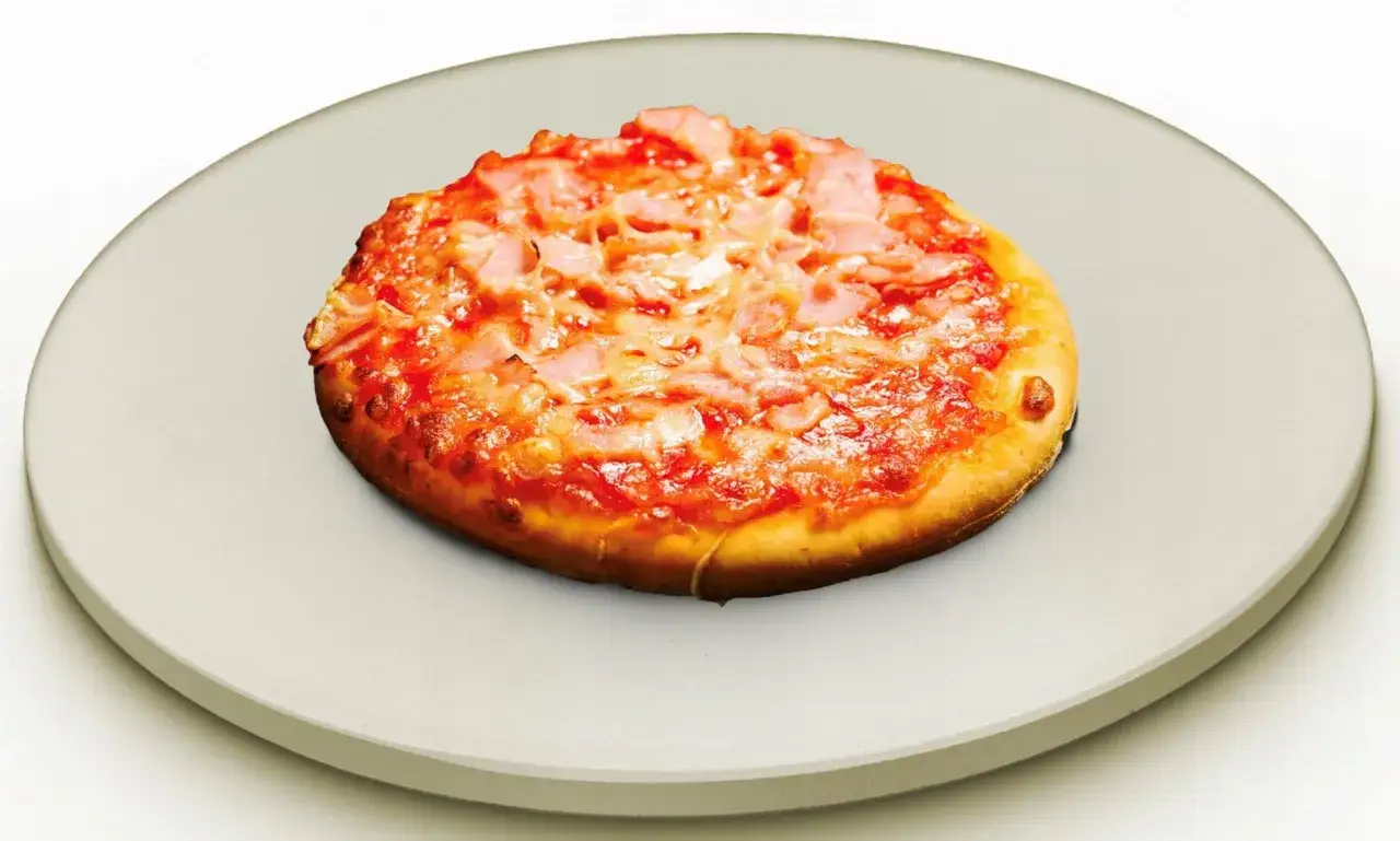 Mała pizza z szynką i serem na okrągłym, jasnym kamieniu. Idealny kamień do pizzy dla domowych wypieków.