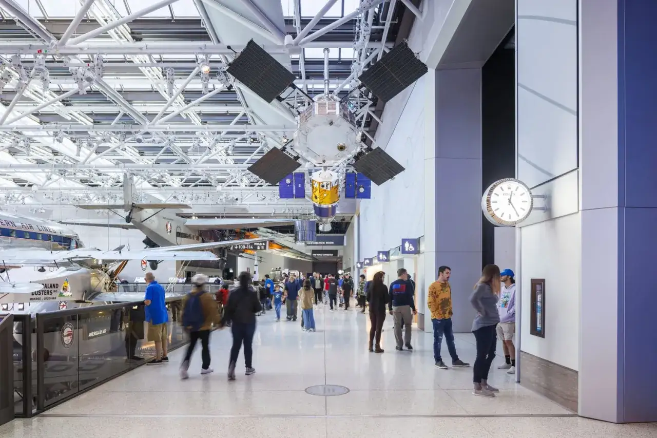 Visitors explore a museum's aviation exhibits, including a satellite and planes, curating meaning from history.