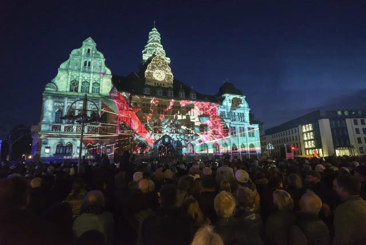 Eine Menschenmenge bestaunt eine beeindruckende Lichtprojektion auf dem Rathaus. Wann ist Recklinghausen leuchtet? Dieses Spektakel findet jährlich statt und verwandelt die Stadt in ein magisches Lichtermeer.