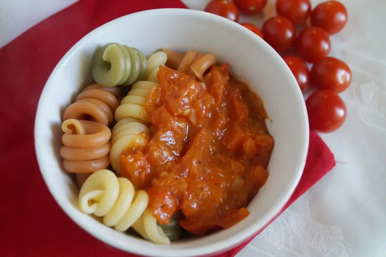 Kolorowy makaron fusilli z pomidorowym sosem do makaronu, obok wiśniowe pomidorki.
