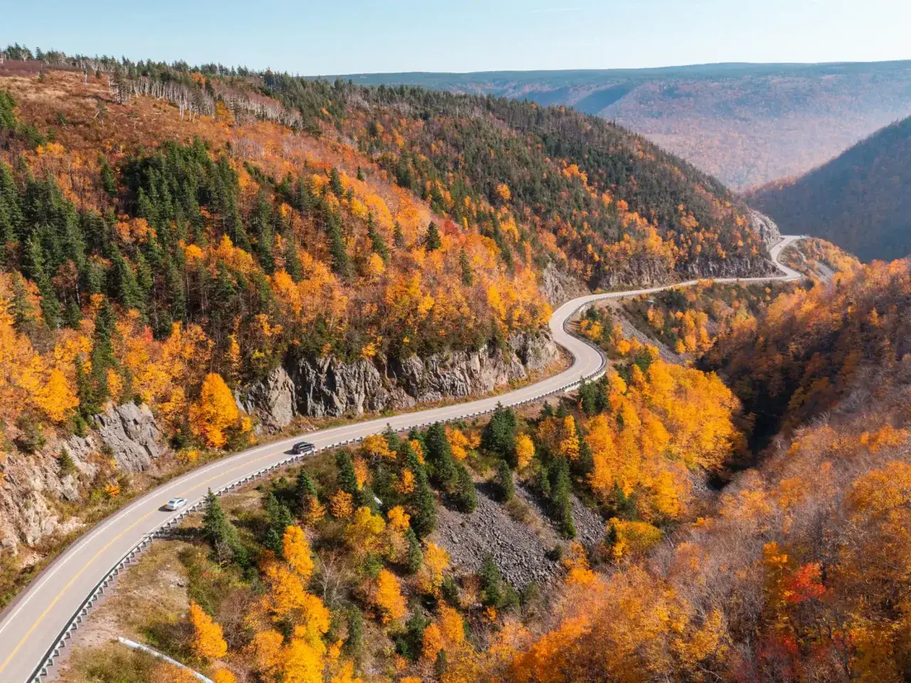 Kurvige Straße durch ein Tal mit leuchtend orangefarbenen Bäumen im Indian Summer in Nova Scotia.