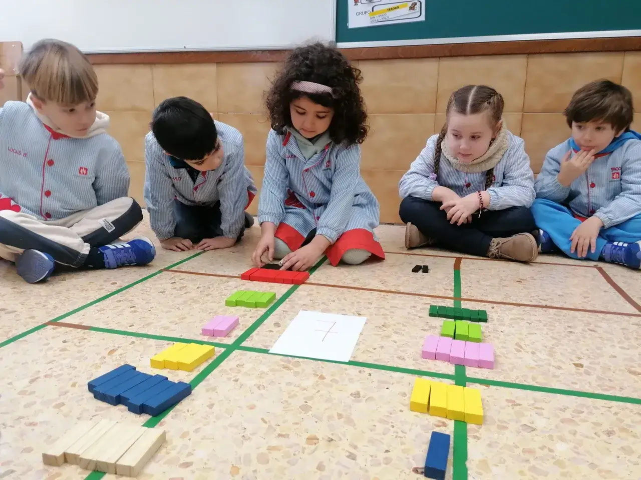 Ni&ntilde;os aprenden matem&aacute;ticas con fichas infantiles. Usan bloques de colores para contar y sumar en el suelo.