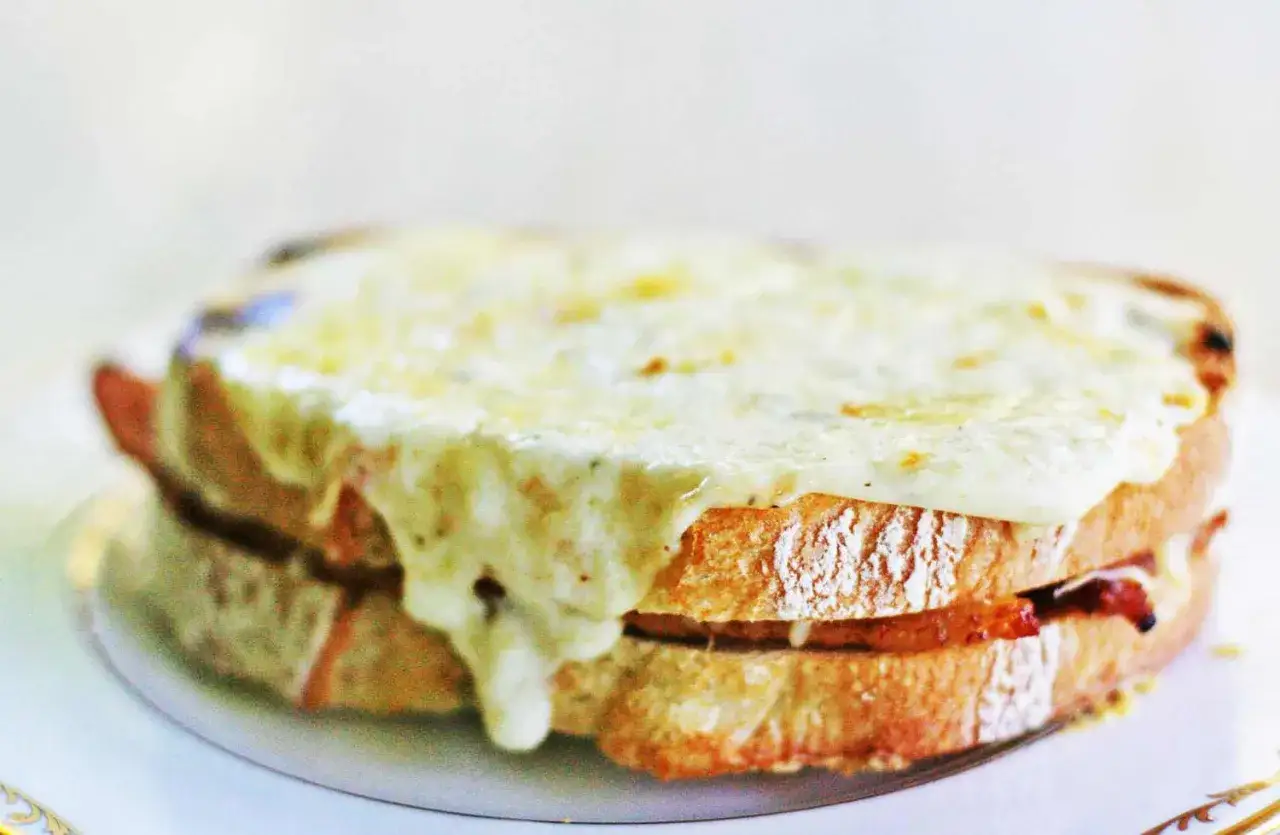 En gyllene, sm&auml;ltande ost t&auml;cker en perfekt rostad croque monsieur, med synliga lager av br&ouml;d och fyllning.