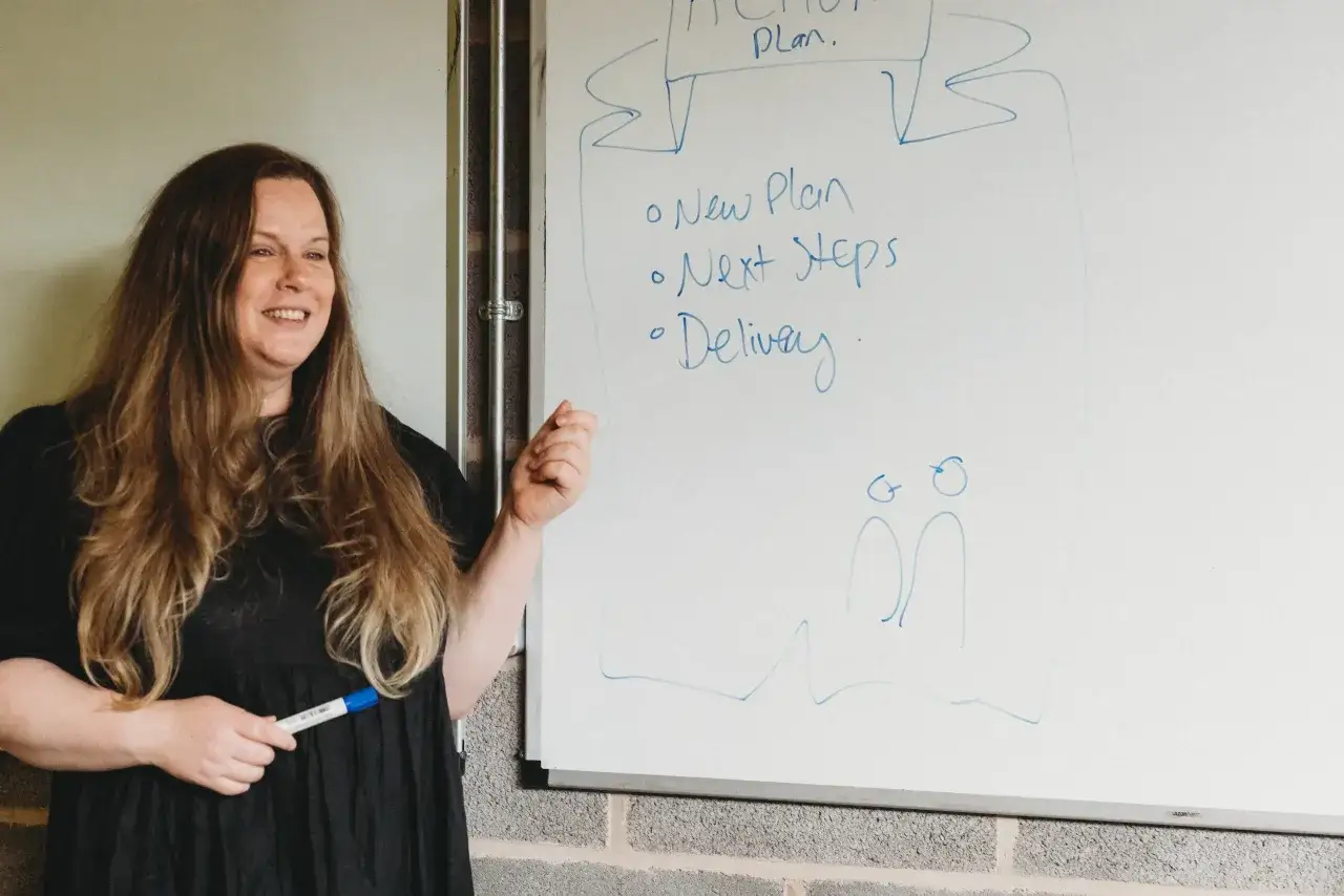 A woman smiles while presenting a whiteboard with