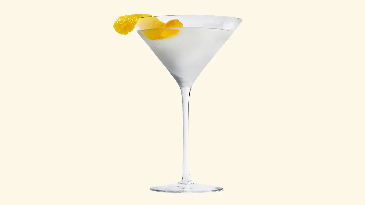 Un verre à cocktail rempli d'un liquide clair, garni d'un zeste de citron. La recette du dry martini est simple et élégante.